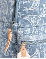 Mochila de denim azul con estampado paisley blanco, bolsillo frontal con cierre, correas regulables y manijas superiores de algodón con broche de cuerina. Acceso mediante cierre superior y puller de cuerina. Incluye tag de cuerina.
