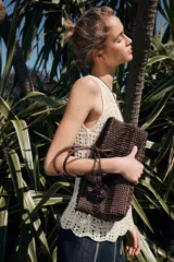Bolso de mano marrón con cuerpo trenzado y doble asa. Incluye charm extraíble y bolsa interior con cierre fruncido.