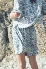 Camisa de corte holgado con estampado de flores azules sobre fondo blanco, cuello clásico, botones frontales y mangas cortas. Confeccionada en sarga con canesú y pliegue en la espalda, hombros caídos y bajo redondeado con aberturas laterales.