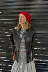 Chaqueta corta de cuero negro con solapas y mangas largas. Presenta flecos colgando en la parte inferior.