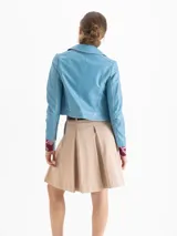 Chaqueta corta de cuero ovino color celeste claro, con cuello solapa, botones forrados y bolsillos aplicados en el frente. Las mangas presentan recortes y forma curvada.