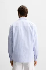 Camisa celeste con rayas verticales blancas, de corte regular, cuello solapa, manga larga con puños abotonados y cierre frontal con botones.