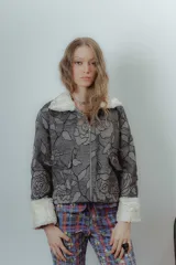 Chaqueta corta gris con estampado floral, cuello y puños de piel sintética blanca y cierre frontal con cremallera.