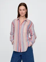 Camisa blanca de muselina con cuello clásico, manga larga y bolsillo en el pecho. Cierre frontal con botones.