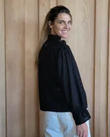 Blusa color beige con cuello con volados, mangas largas abullonadas con puños elásticos y cierre con botones en la parte delantera.