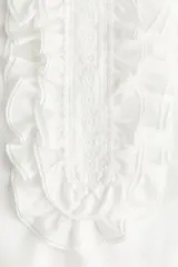 Blusa blanca sin mangas con cuello mao y pechera de volados con bordados de encaje.