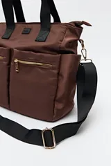 Bolso tote marrón de nylon con doble asa de mano negra y correa bandolera negra regulable y desmontable. Tiene dos bolsillos frontales con cierre metálico dorado.