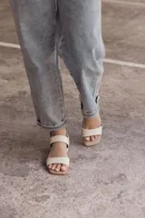 Sandalia de cuero color beige claro (off white) con taco ancho y tiras finas ajustables con hebilla metálica dorada en el tobillo.