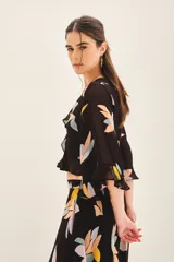 Camisa crop de manga larga con volados en mangas y cintura, confeccionada en viscosa georgette estampada con motivos florales abstractos en tonos pastel sobre fondo negro.