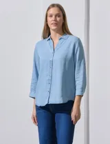Camisa celeste de tencel con cuello con solapa, escote en V, abertura central con botones y mangas 3/4 regulables con presilla y botón.