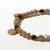 Pulsera elástica con cuentas facetadas color beige, separadores dorados, cuentas cuadradas de madera marrón y dijes redondos dorados.