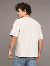 Remera color crema de corte holgado, confeccionada en tejido interlock de algodón y elastano. Presenta cuello redondo y logo CK bordado en el pecho.