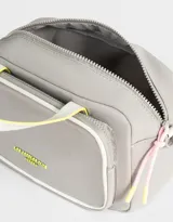 Cartera bowling gris claro de tela deportiva con bolsillo frontal y tag de goma. Tiene correa regulable desmontable, manijas superiores, cierre superior, bolsillo frontal con cierre y puller de cordón y goma, y mosquetón lateral con cordones decorativos.