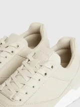 Zapatillas urbanas color beige, confeccionadas en cuero y tela, con suela blanca y cordones. Presentan monograma de la marca en el lateral.