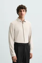 Camisa color beige de corte slim fit, confeccionada en tejido elástico con cuello italiano abierto, manga larga con puños abotonados y cierre frontal con botones.