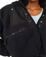 Chaqueta de polar suave color beige, con silueta ligeramente oversize. Presenta cierre frontal con botones a presión, bolsillos laterales con cremallera y parches decorativos de nailon en el frente.