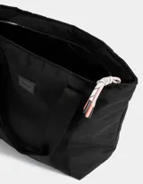 Bolso negro tipo shopper de tela deportiva con doble asa de hombro, cierre superior con tirador de cordón y goma, y etiqueta de goma con logo.
