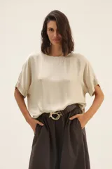 Blusa color beige de raso con ribete de lurex y mangas cortas.