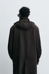 Trench relaxed fit negro confeccionado en tejido técnico ligeramente acolchado, con cuello subido y capucha desmontable. Tiene manga larga, bolsillos de vivo en pecho y de solapa en cadera, y abertura en el centro de la espalda. El cierre frontal es con cremallera oculta por solapa con botones a presión.