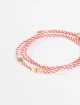Pulsera de cordón rojo y blanco con dijes metálicos dorados en forma de corazón y tréboles.