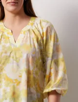 Blusa de gasa verde con estampado de flores blancas y celestes. Tiene cuello a la base con escote en V y mangas 3/4 fruncidas.