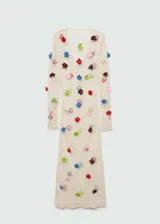 Vestido largo de tejido de punto calado color crudo, con escote en V y mangas largas. Presenta detalles de flores multicolores aplicadas.