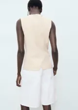 Chaleco color crema con cuello redondo y cierre frontal con botones.