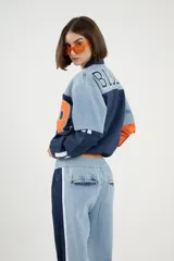 Campera corta estilo sporty chic con cierre frontal, confeccionada en denim celeste y tejido técnico azul y naranja. Presenta diseño color-block y corte holgado.