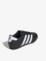 Zapatillas Adidas de cuero negro con las tres rayas blancas y suela color caramelo.