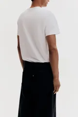 Remera blanca de algodón liviano con cuello redondo ribeteado y bajo recto. Corte ajustado que realza el contorno del cuerpo creando una silueta entallada.