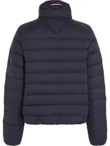 Campera acolchada azul marino con cuello alto, cierre frontal con cremallera y bolsillos laterales con ojal. Presenta detalles distintivos de la marca Tommy Hilfiger, como la cinta con los colores de la marca en el cierre y el logo bordado en el pecho.