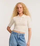 Blusa de punto color crema, con cuello polo, mangas cortas y puños con botones.