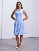 Vestido midi de lunares blancos sobre fondo celeste, marca Sandra Darren. Tiene cuello alto cruzado con abertura ojal y aplique metálico. Corte en la cintura y falda acampanada. Sin mangas.