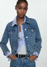 Chaqueta de jean azul de corte clásico con cuello de solapa, cierre frontal con botones metálicos, bolsillos delanteros con solapa y puños abotonados.