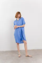 Vestido camisero corto color verde oliva, confeccionado en lino 100%. Tiene botones en la parte delantera, cuello camisero, mangas cortas con botón para arremangar y bolsillos laterales.