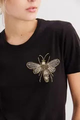Remera negra de algodón con calce al cuerpo, mangas cortas y cuello redondo. Presenta un bordado frontal de abeja con canutillos dorados y plateados.