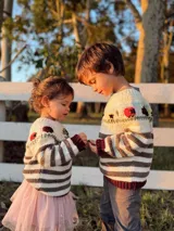 Sweater tejido y bordado a mano en 100% lana merino, con cuello redondo y diseño de rayas horizontales en tonos crudo y marrón. Presenta bordados de animales y flores en la parte superior.