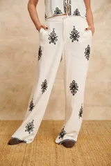 Pantalón de lino color crema con bordados florales negros.