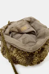 Mini bolso tipo saca de tela color beige con bordados florales y detalles de lentejuelas y mostacillas en tonos dorados y marrones. Posee asa de hombro hecha de mostacillas doradas y borde festoneado con mostacillas.
