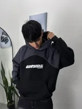 Buzo con capucha combinado en negro y gris, con bolsillo tipo canguro y logo estampado en el pecho.