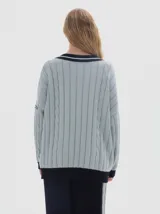 Buzo tejido oversized color celeste, con cuello en V y ribetes negros y blancos. Presenta mangas largas con diseño de trenzas y puños y dobladillo acanalados en color negro.