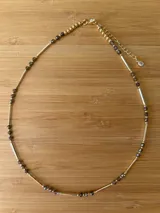Gargantilla dorada con cuentas facetadas color gris oscuro y tubos dorados.