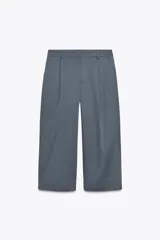 Pantalón corto gris de tiro alto con pinzas delanteras, bolsillos laterales y traseros. Cierre frontal con cremallera y gancho metálico.