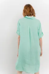 Vestido camisero corto color verde oliva, confeccionado en lino 100%. Tiene botones en la parte delantera, cuello camisero, mangas cortas con botón para arremangar y bolsillos laterales.