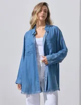 Camisa de jean celeste, marca Hester & Orchand, de corte oversize con cuello con solapa, escote en V y abertura central con botones. Delantera con bolsillos aplicados, mangas largas regulables con presilla y botón, y ruedo desflecado.