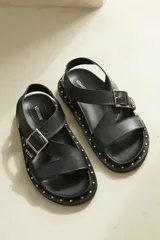 Sandalias negras de cuero con suela track, detalle de tachas plateadas y ajuste con hebilla metálica.