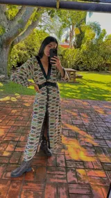 Vestido largo tipo abrigo, color azul, con estampado geométrico en tonos tierra, cuello en V con ribete negro, botones frontales y cinturón negro a la cintura.