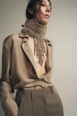 Collar tipo babero con flecos de piezas metálicas doradas y cadena de eslabones negros.