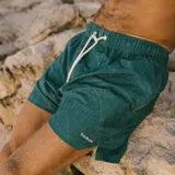 Short de baño verde con estampado de hojas en blanco. Tiene cintura elástica con cordón ajustable y logo de la marca en la pierna izquierda.
