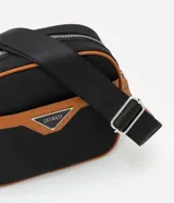 Cartera bandolera negra con detalles en marrón, confeccionada en poliéster certificado Grs y poliuretano. Presenta un aplique metálico triangular, asa larga ajustable y cierre por cremallera.